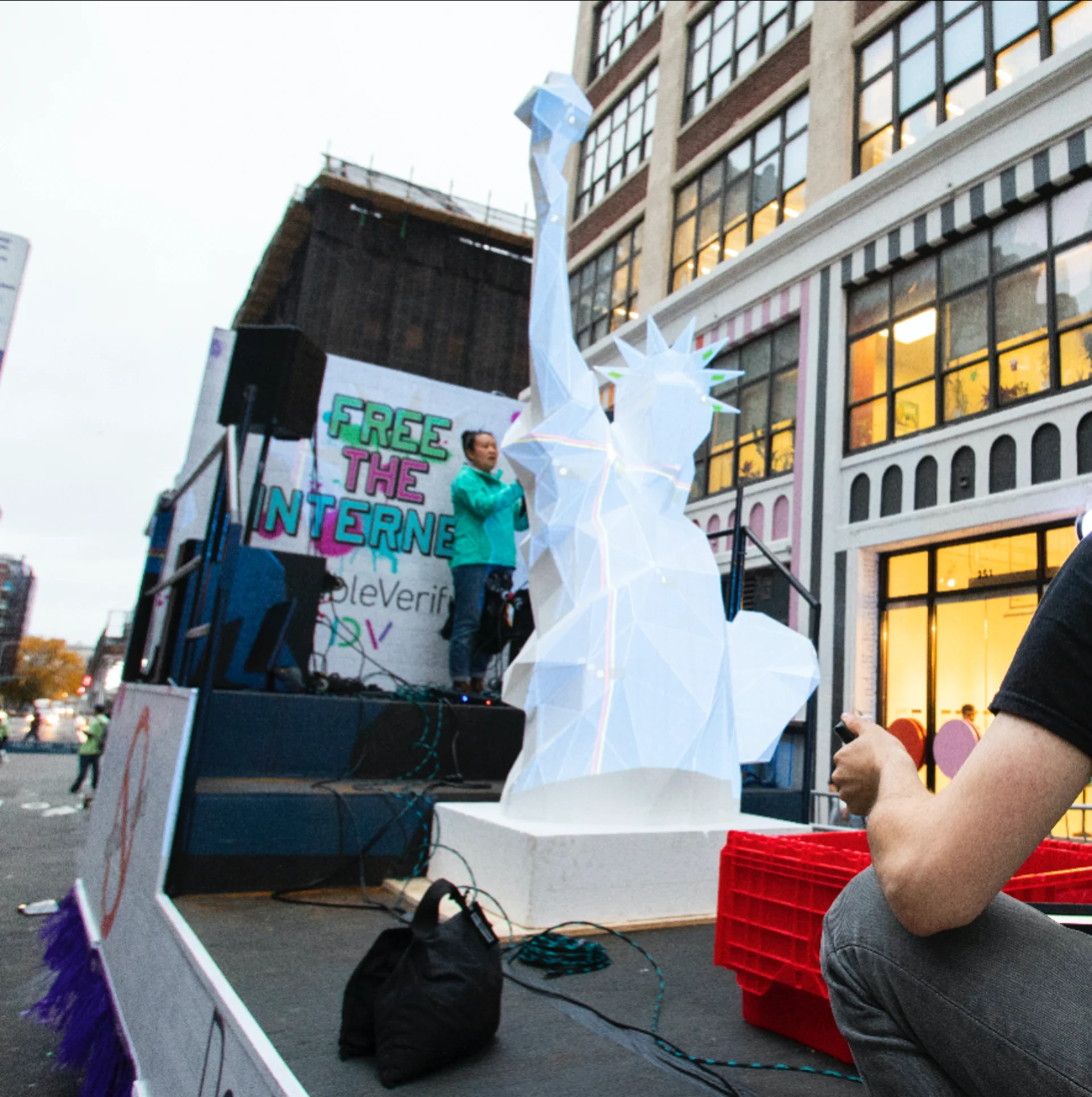 DoubleVerify : le char avant la nuit, la statue blanche en facettes sur le plateau du camion, la bannière « Free the Internet » et une oratrice au micro