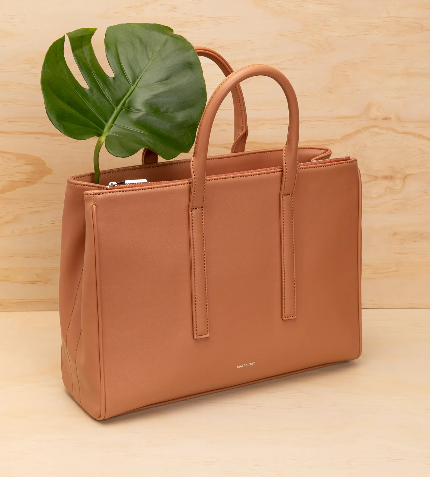 Matt & Nat : un cabas camel et une feuille de monstera, sur fond de bois clair