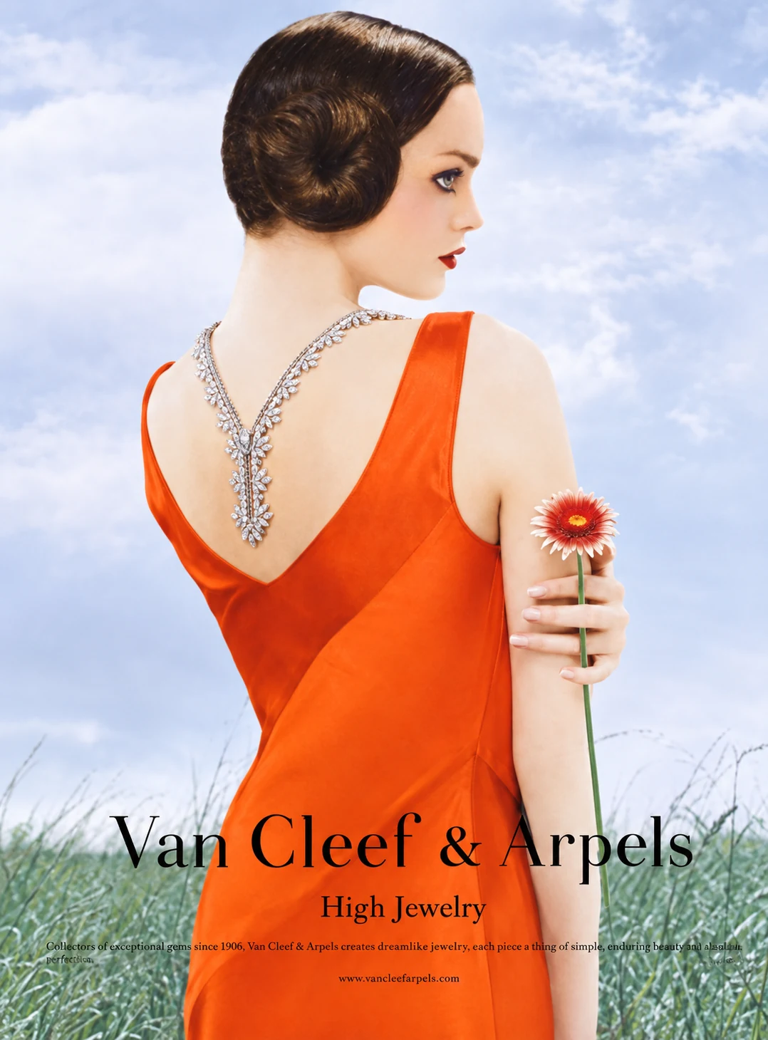 La campagne photographiée : un mannequin de dos en robe orange, collier de diamants et gerbera rouge.