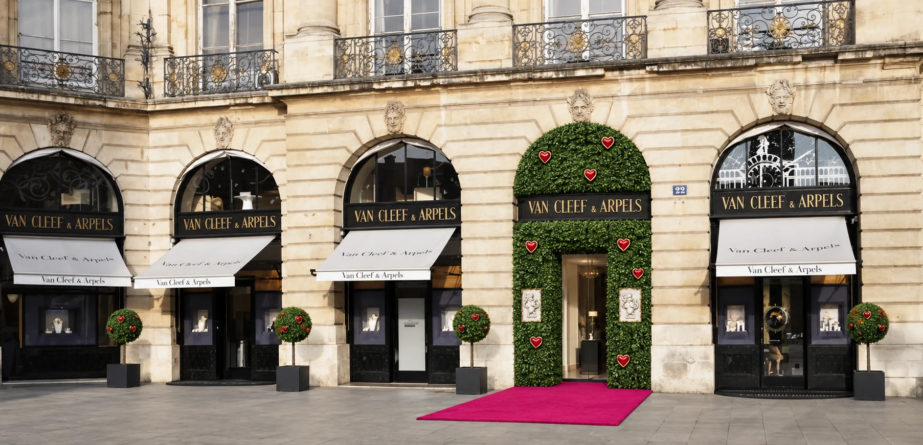 Van Cleef & Arpels, place Vendôme : la porte de la boutique encadrée d'une arche de feuillage semée de cœurs rouges, des arbres en pot devant chaque vitrine et un tapis rose.