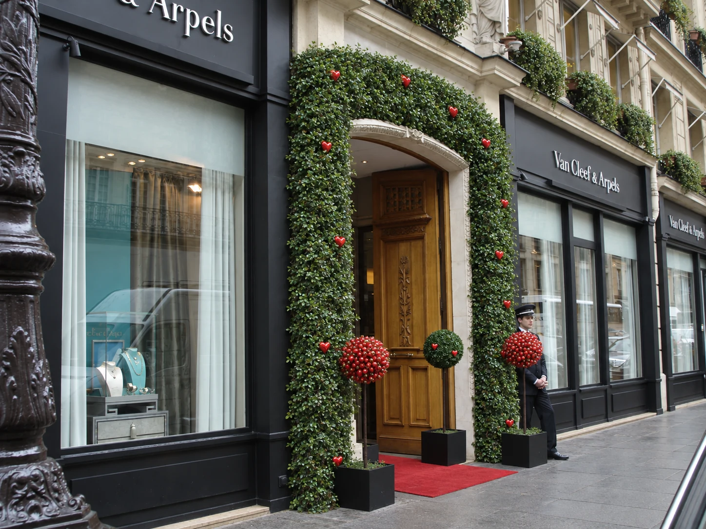 Van Cleef & Arpels, rue de la Paix : l'entrée de la boutique habillée d'une arche de feuillage semée de cœurs rouges, deux arbres en pot et un tapis rouge.